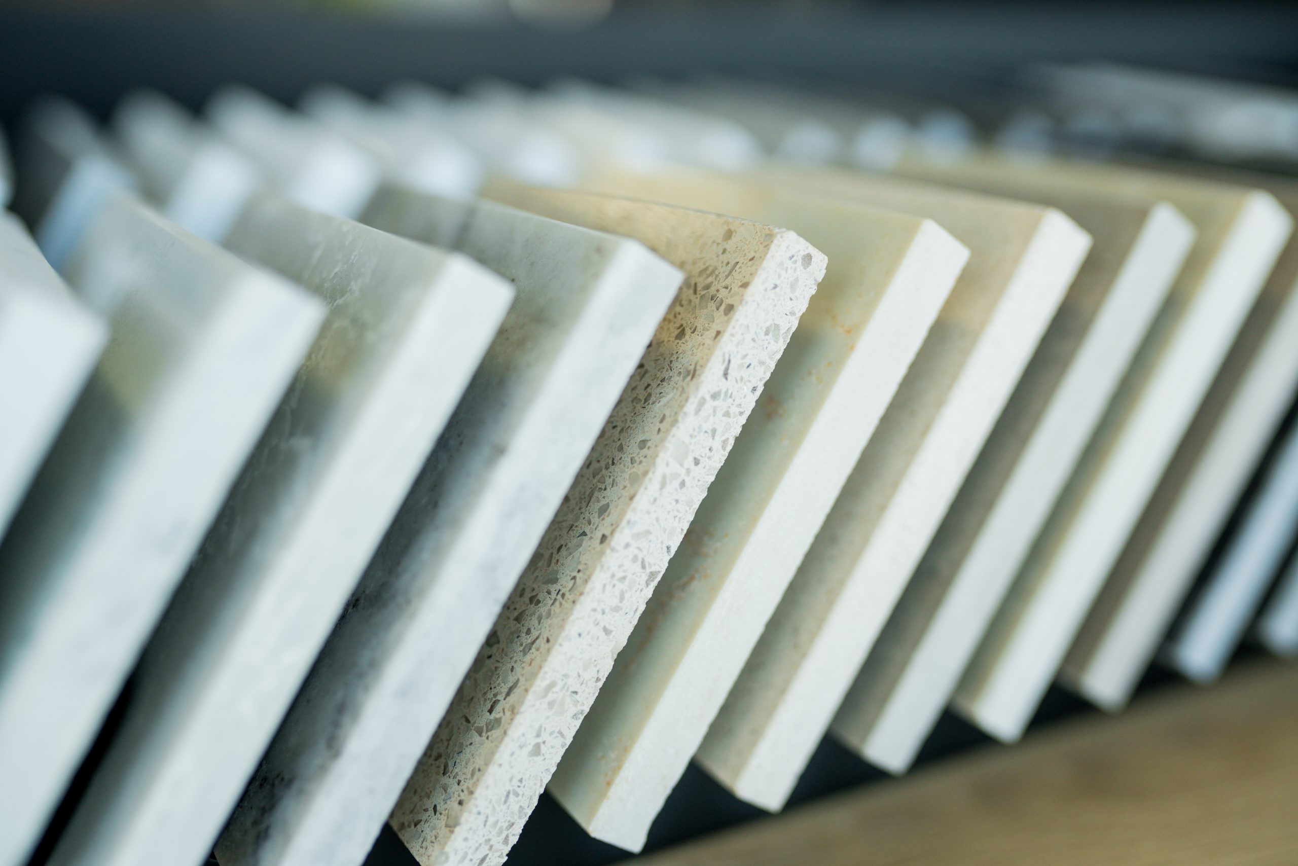 Quartz countertop slab samples in a kitchen design showroom alongside other stone surfaces, illustrating the buying-decision moment around a proposed engineered-quartz tariff.