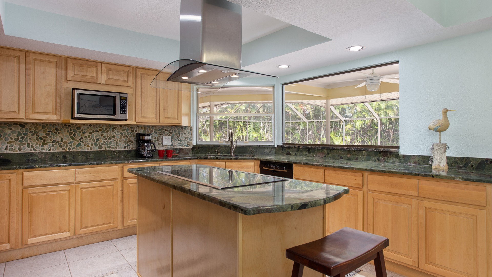 Kitchen with green granite countertops on the perimeter and a center island below natural wood cabinets