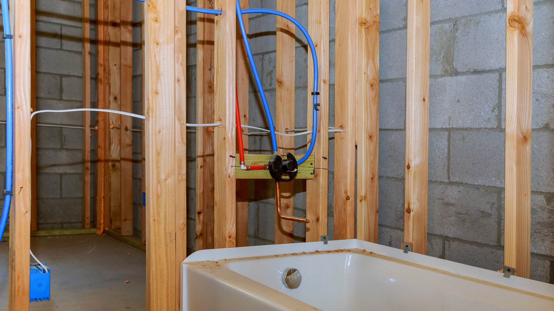 Bathroom alcove with the bathtub removed, showing the exposed subfloor and open shower drain rough-in