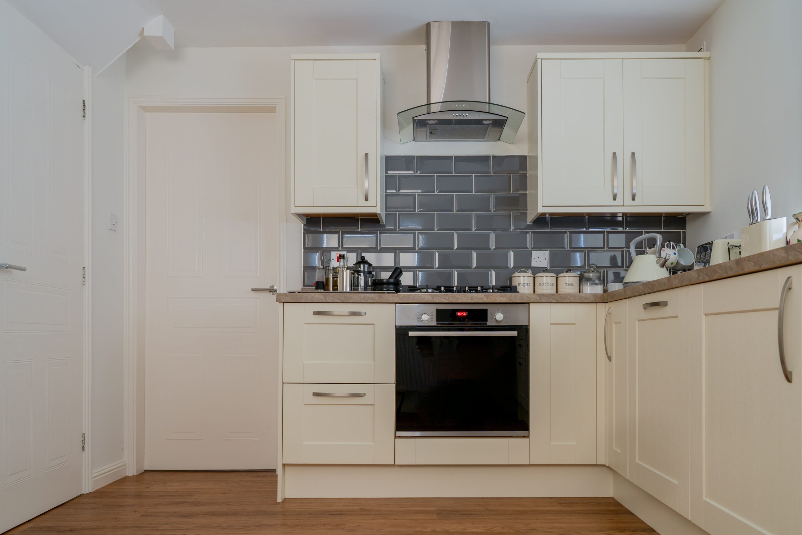 Stainless steel chimney range hood mounted above a gas cooktop in a cream shaker kitchen