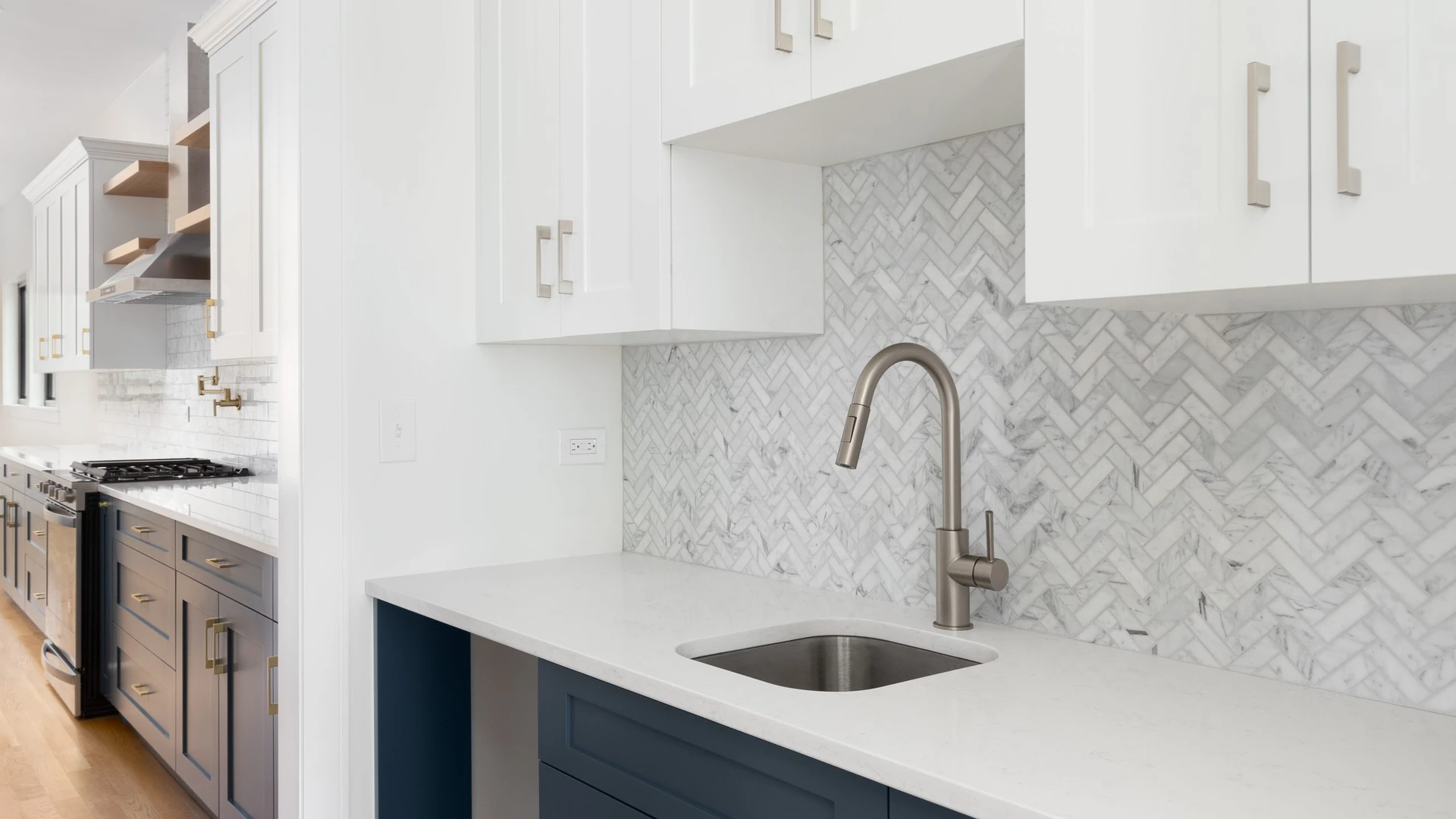 Arched metallic faucet above an undermount sink, with a pale herringbone backsplash and white upper cabinets.