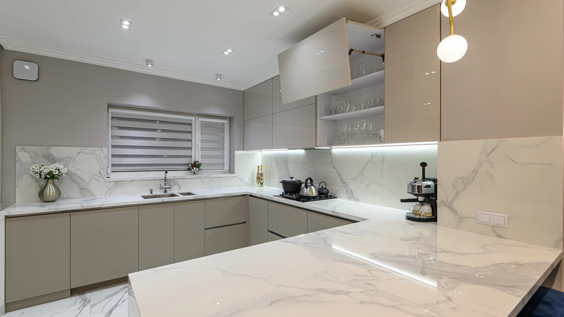 Kitchen with pale veined countertops and backsplash above taupe cabinets.