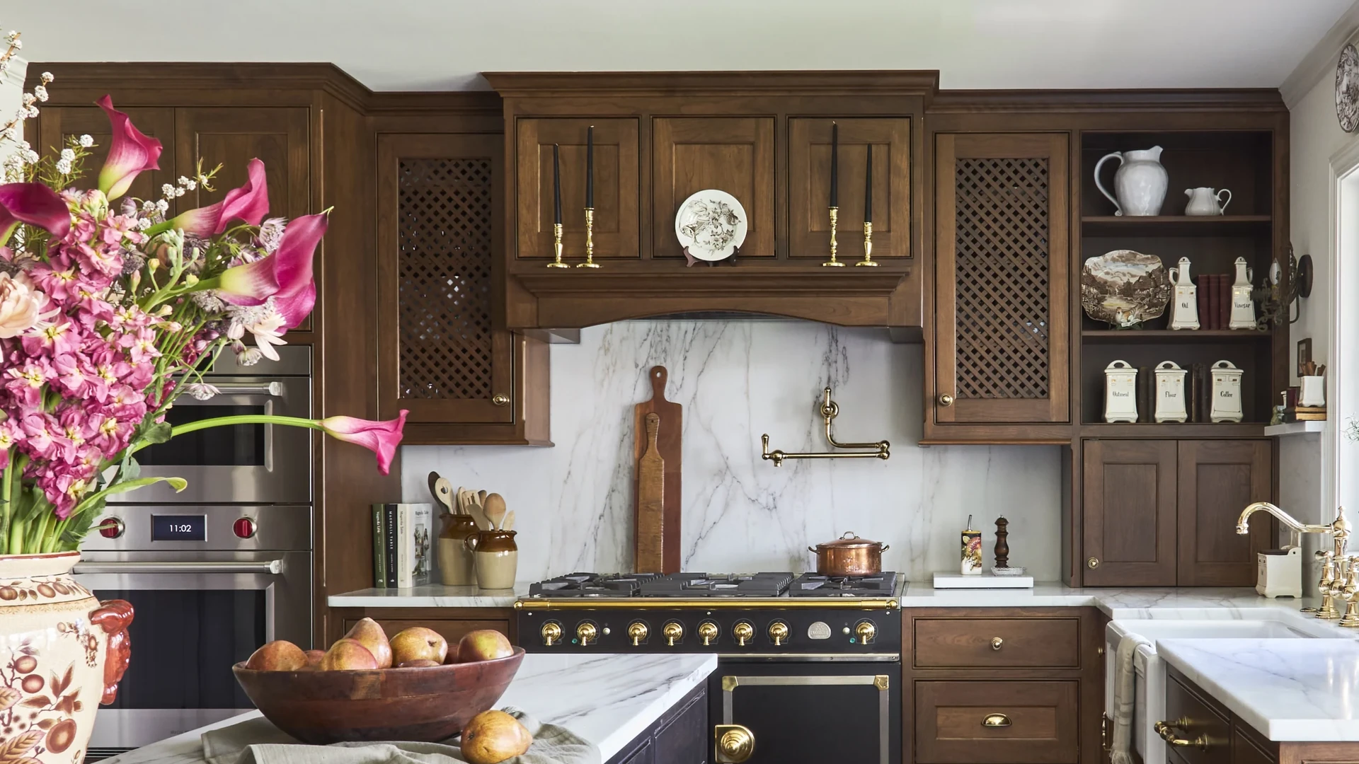 Brown wood hood with three raised panels above a black range with brass knobs, flanked by matching cabinets and a marble backsplash